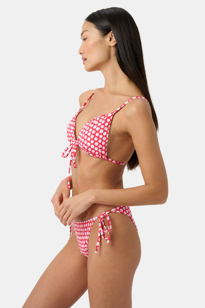 A woman wears the Roller Rabbit Starry Dot Isa Bikini Top, a red triangle bikini with white polka dots and a front tie, shown from shoulders to waist against a plain background.