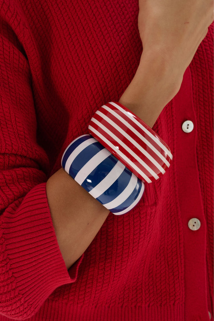 The Roller Rabbit Striped Bangle is a wide, round wooden bracelet with a glossy red finish and evenly spaced hand-painted white stripes, shown on a plain light gray background.