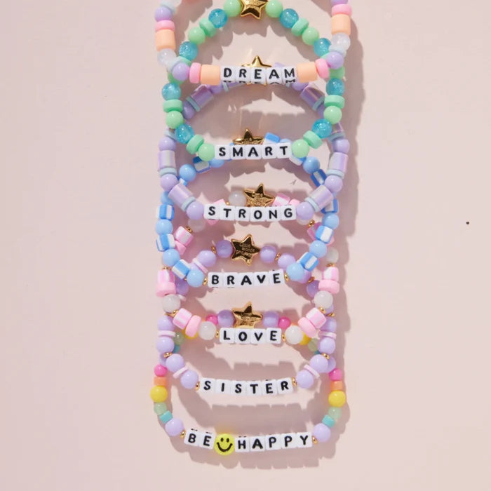 Colorful beaded bracelets with motivational phrases on a light pink background