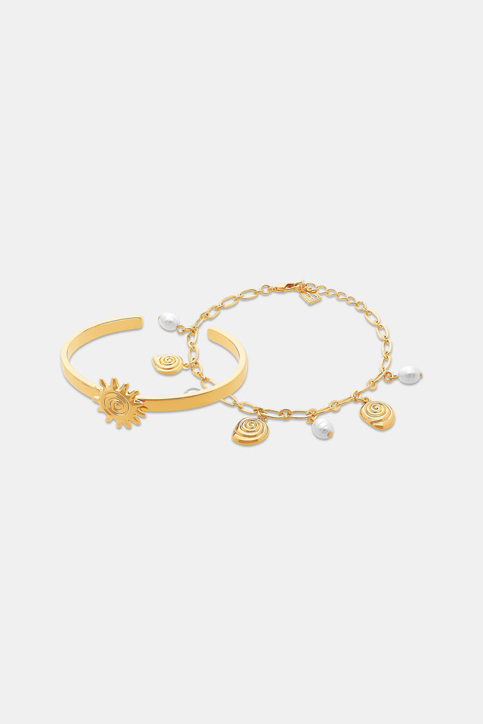 The Roller Rabbit Sun Charms Citra Bracelet Stack features a gold cuff with a sun-shaped charm and a gold chain bracelet adorned with swirl designs and pearl-like charms, both displayed on a plain white background.
