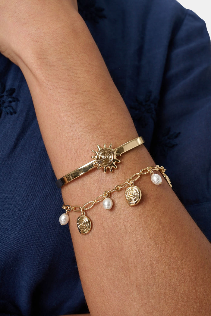 The Roller Rabbit Sun Charms Citra Bracelet Stack features a gold cuff with a sun-shaped charm and a gold chain bracelet adorned with swirl designs and pearl-like charms, both displayed on a plain white background.
