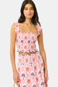 A woman wears the Roller Rabbit Sunny Days Sabrina Top, a cropped, sleeveless ruffled pink and white piece paired with a matching high-waisted skirt in a pink and orange geometric floral linen-viscose blend, standing before a plain light background.