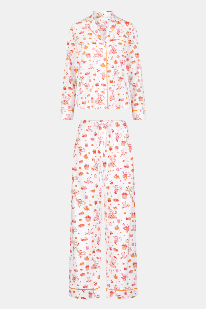 A woman stands barefoot against a plain white background, hands in pockets, wearing the Roller Rabbit Sweater Weather Long Sleeve Polo Pajamas—a floral pink and white set featuring a long-sleeved polo top and matching pants.