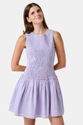 A young girl wearing the Roller Rabbit Kids Sweet Stripe Casey Dress stands in front of lockers, smiling and holding a folder decorated with colorful raindrops.