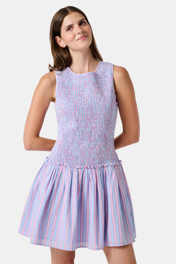A young girl wearing the Roller Rabbit Kids Sweet Stripe Casey Dress stands in front of lockers, smiling and holding a folder decorated with colorful raindrops.
