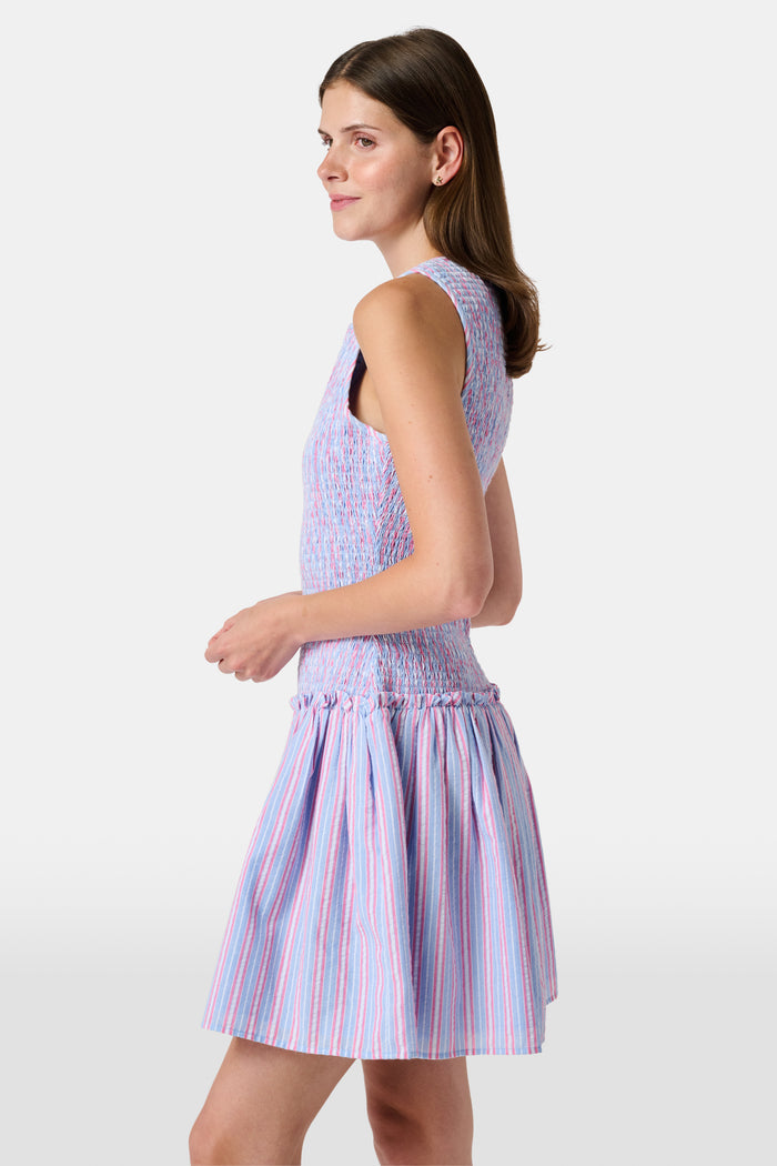 A young girl wearing the Roller Rabbit Kids Sweet Stripe Casey Dress stands in front of lockers, smiling and holding a folder decorated with colorful raindrops.