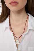 A woman wears a white shirt and the Roller Rabbit Swirl Cord Necklace—a red cord with a silver shell pendant. Only her lower face, neck, and upper chest are visible.