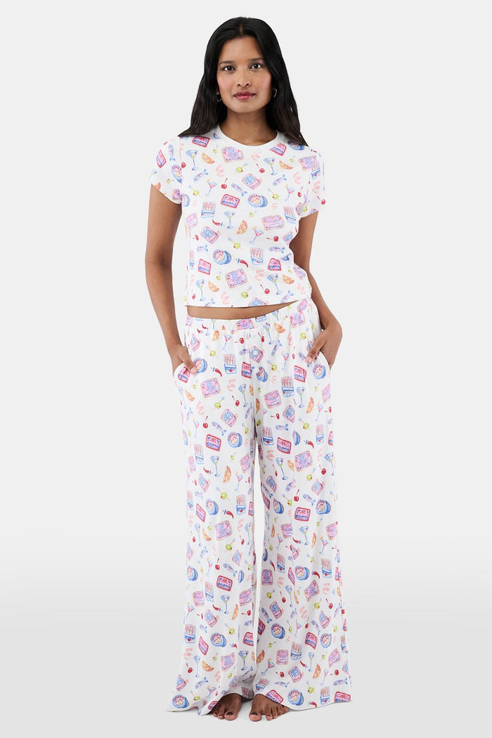 A person wears the Roller Rabbit Tinned or Twist Boden Pant, ultra-soft and white with playful prints. Their matching top complements the wide-leg pull-on pants, and they are barefoot.