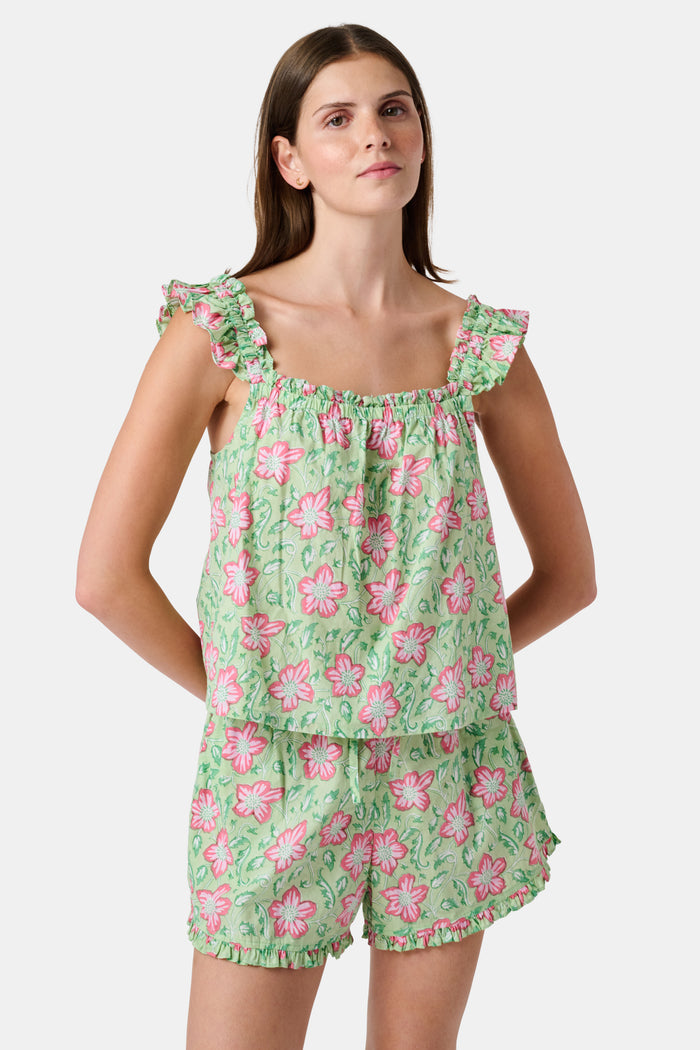 Three women are in a library. One wears the Verdant Floral Pipette Dress by Roller Rabbit—a green floral minidress—and stands with her hand on her chin. Another sits on a patterned sofa with her eyes closed, and bookshelves are visible in the background.