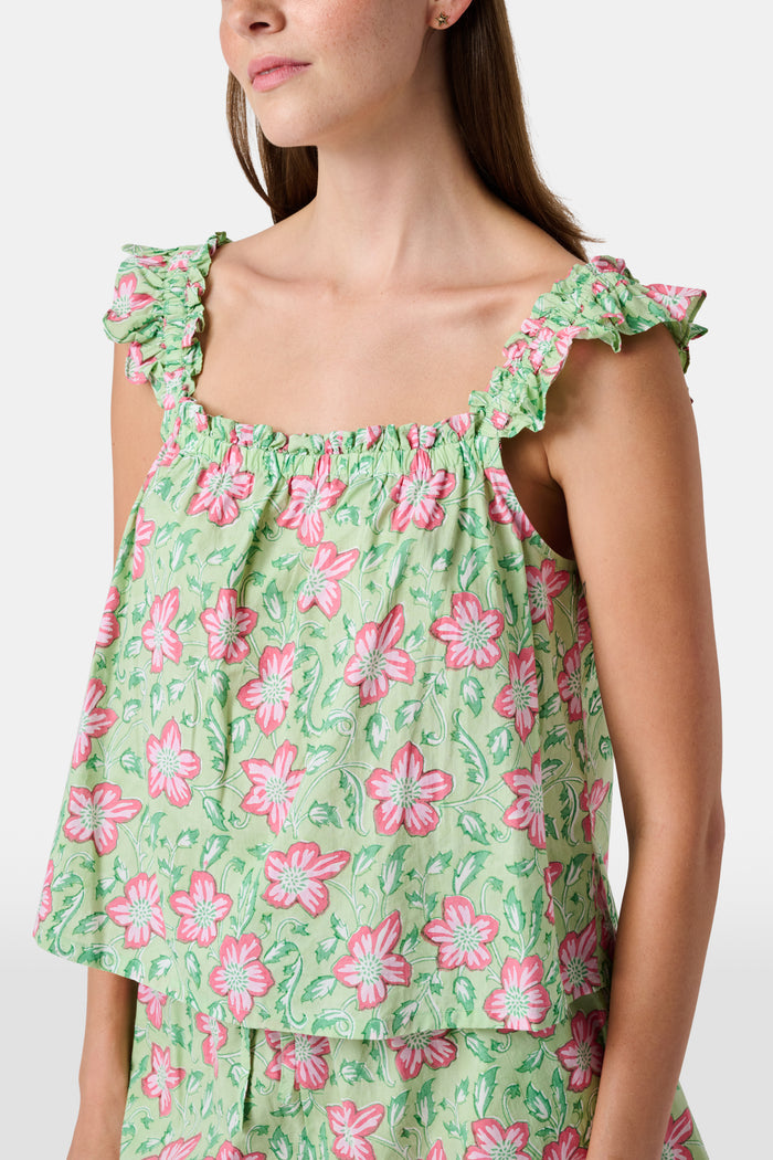 Three women are in a library. One wears the Verdant Floral Pipette Dress by Roller Rabbit—a green floral minidress—and stands with her hand on her chin. Another sits on a patterned sofa with her eyes closed, and bookshelves are visible in the background.