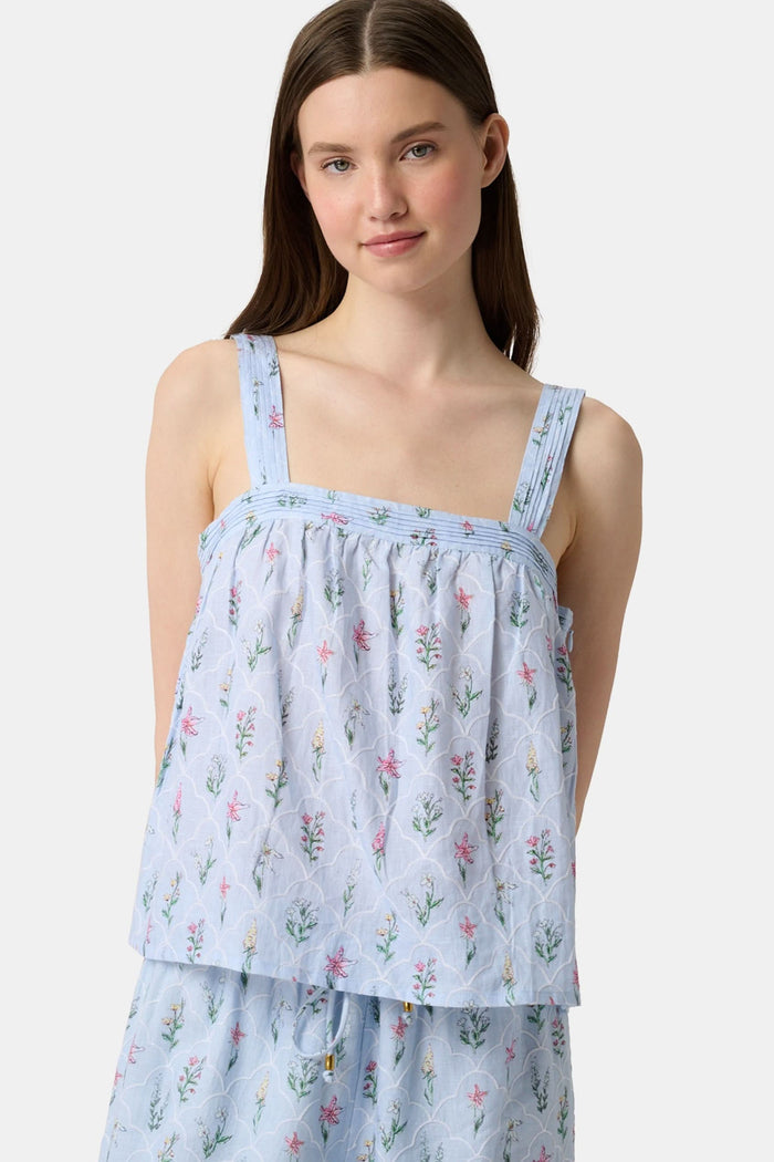 A woman with long brown hair wears the Roller Rabbit Wildflower Jemina Victoria Top, a sleeveless baby blue linen piece with wide shoulder straps, standing against a plain light background.