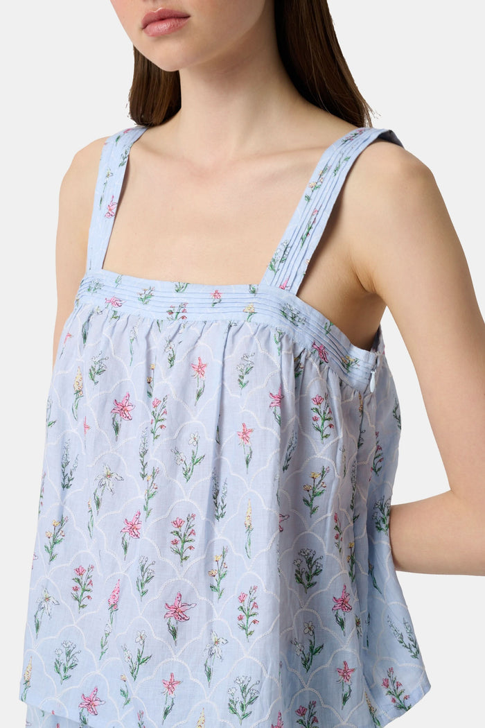 A woman with long brown hair wears the Roller Rabbit Wildflower Jemina Victoria Top, a sleeveless baby blue linen piece with wide shoulder straps, standing against a plain light background.