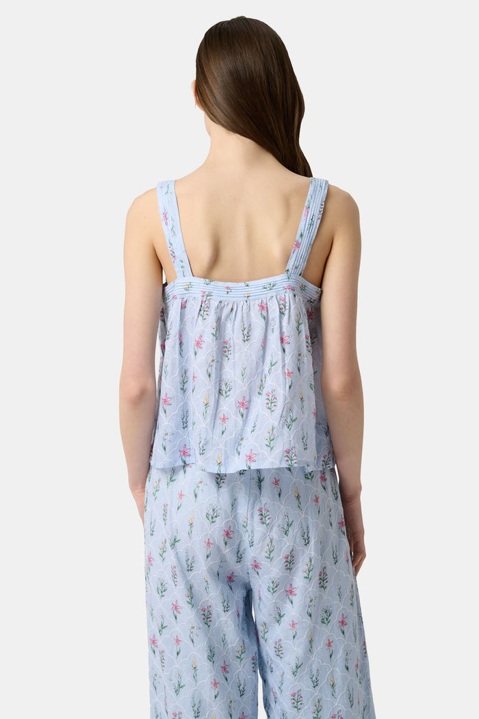 A woman with long brown hair wears the Roller Rabbit Wildflower Jemina Victoria Top, a sleeveless baby blue linen piece with wide shoulder straps, standing against a plain light background.