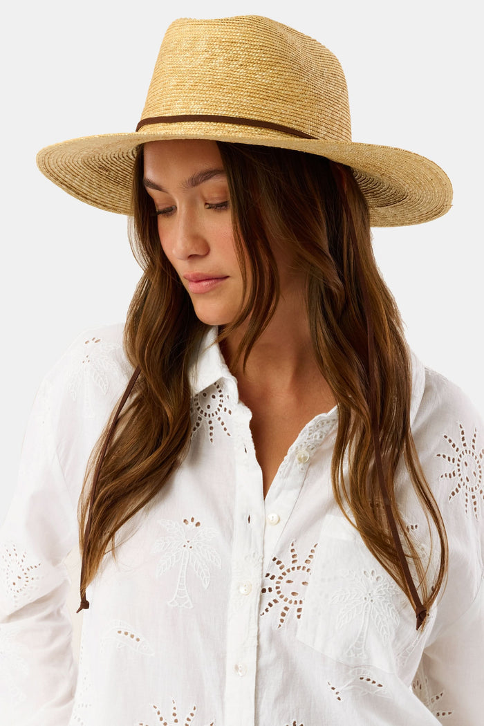 A woman with long brown hair wears the Hat Attack Willow Mini Surfer Hat and a white embroidered button-up shirt, looking down with a gentle expression against a plain background.