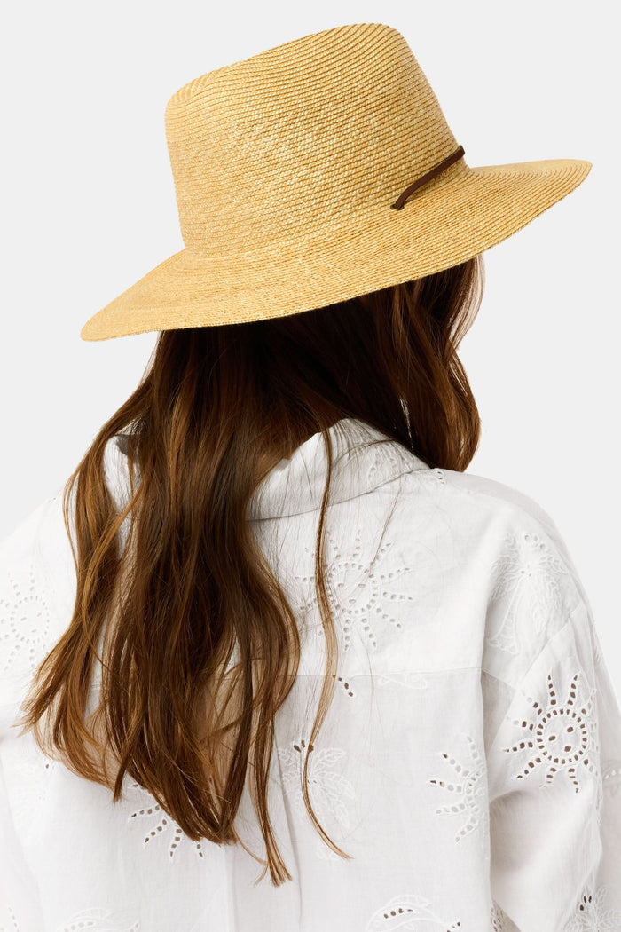 A woman with long brown hair wears the Hat Attack Willow Mini Surfer Hat and a white embroidered button-up shirt, looking down with a gentle expression against a plain background.