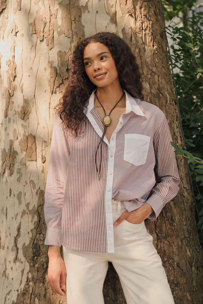 A woman wearing the Roller Rabbit Yarn Dye Stripe Emory Dress—a cotton button-down style with a tie belt and white collar—smiles while looking to the side and pairs the dress with knee-high boots. The background is plain light gray.