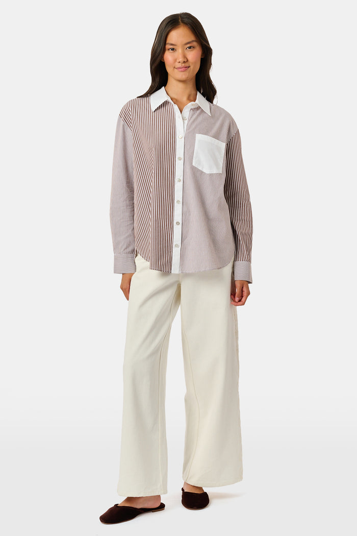 A woman wearing the Roller Rabbit Yarn Dye Stripe Emory Dress—a cotton button-down style with a tie belt and white collar—smiles while looking to the side and pairs the dress with knee-high boots. The background is plain light gray.
