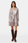 A woman wearing the Roller Rabbit Yarn Dye Stripe Emory Dress—a cotton button-down style with a tie belt and white collar—smiles while looking to the side and pairs the dress with knee-high boots. The background is plain light gray.