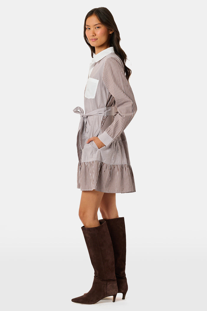 A woman wearing the Roller Rabbit Yarn Dye Stripe Emory Dress—a cotton button-down style with a tie belt and white collar—smiles while looking to the side and pairs the dress with knee-high boots. The background is plain light gray.