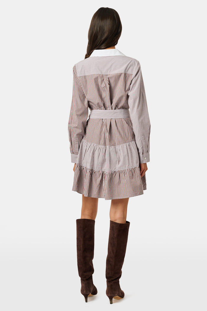 A woman wearing the Roller Rabbit Yarn Dye Stripe Emory Dress—a cotton button-down style with a tie belt and white collar—smiles while looking to the side and pairs the dress with knee-high boots. The background is plain light gray.