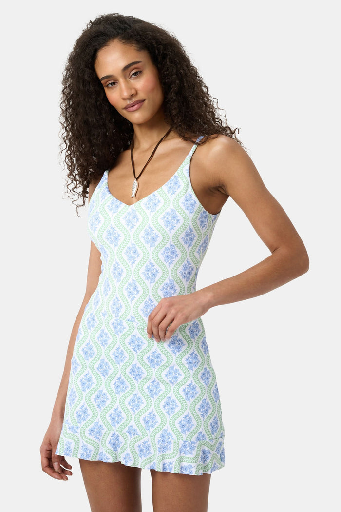 A woman in the Roller Rabbit Zelda Floral Larissa Swim Skirt stands smiling by a marina, sporting long curly hair and enjoying stylish sun protection from her outfit.
