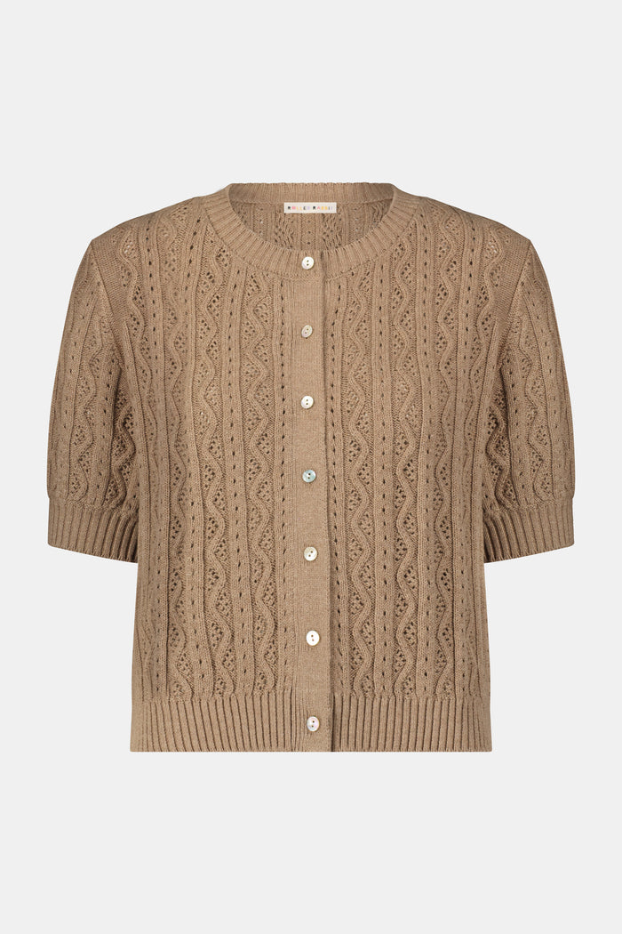 A woman wears the Roller Rabbit Zig Zag Pointelle Nyla Cardigan, a short-sleeved, walnut brown button-front sweater with circular patterns, paired with a light blue patterned skirt.